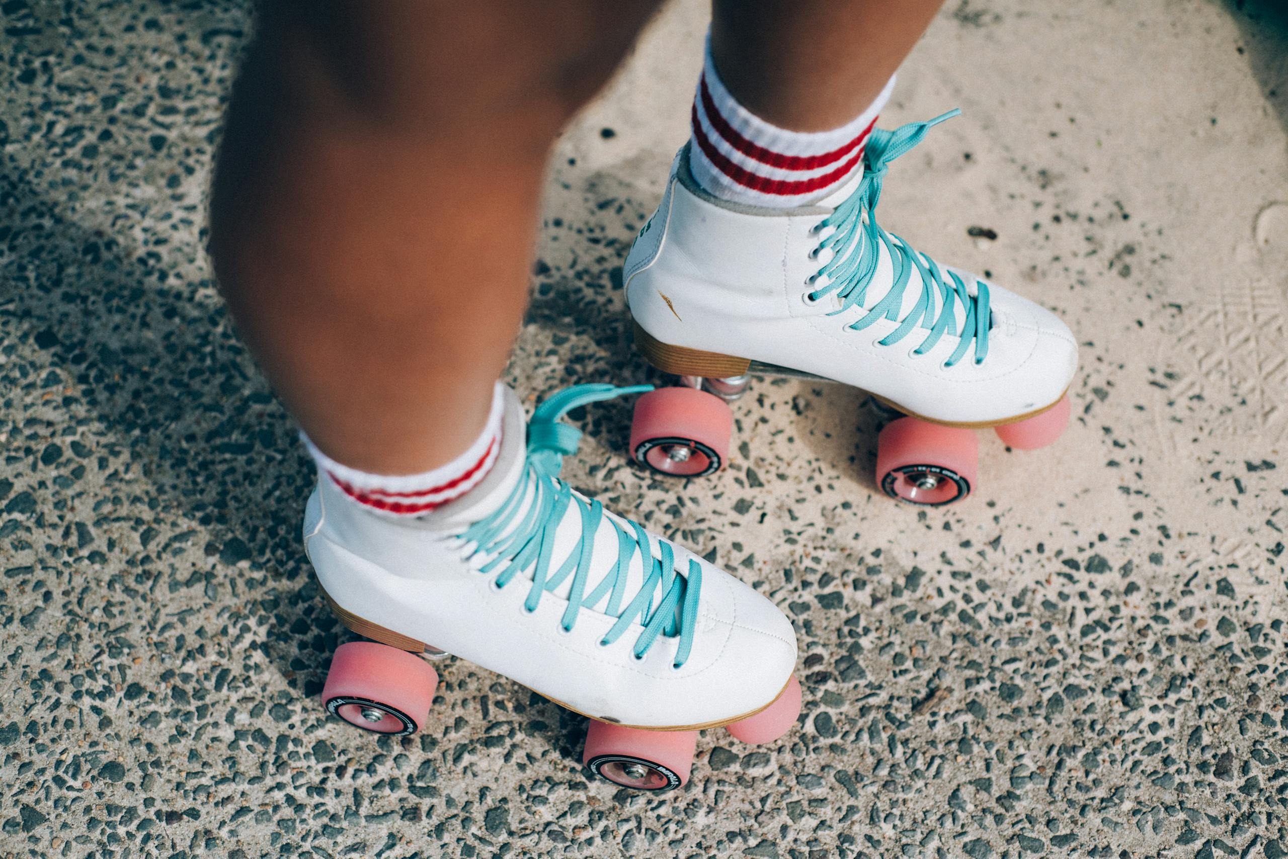 Photo of person's legs wearing white and red socks with white roller skates, red wheels and aqua laces on concrete floor